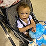 Kaelee joined the competition — help win amazing prizes! toddler, child, stroller, stuffed_toy, blue, floor, tile, blanket, curly_hair, clothing, indoor, seat, person, baby, hand, expression, toy, sitting, young_child, looking_up