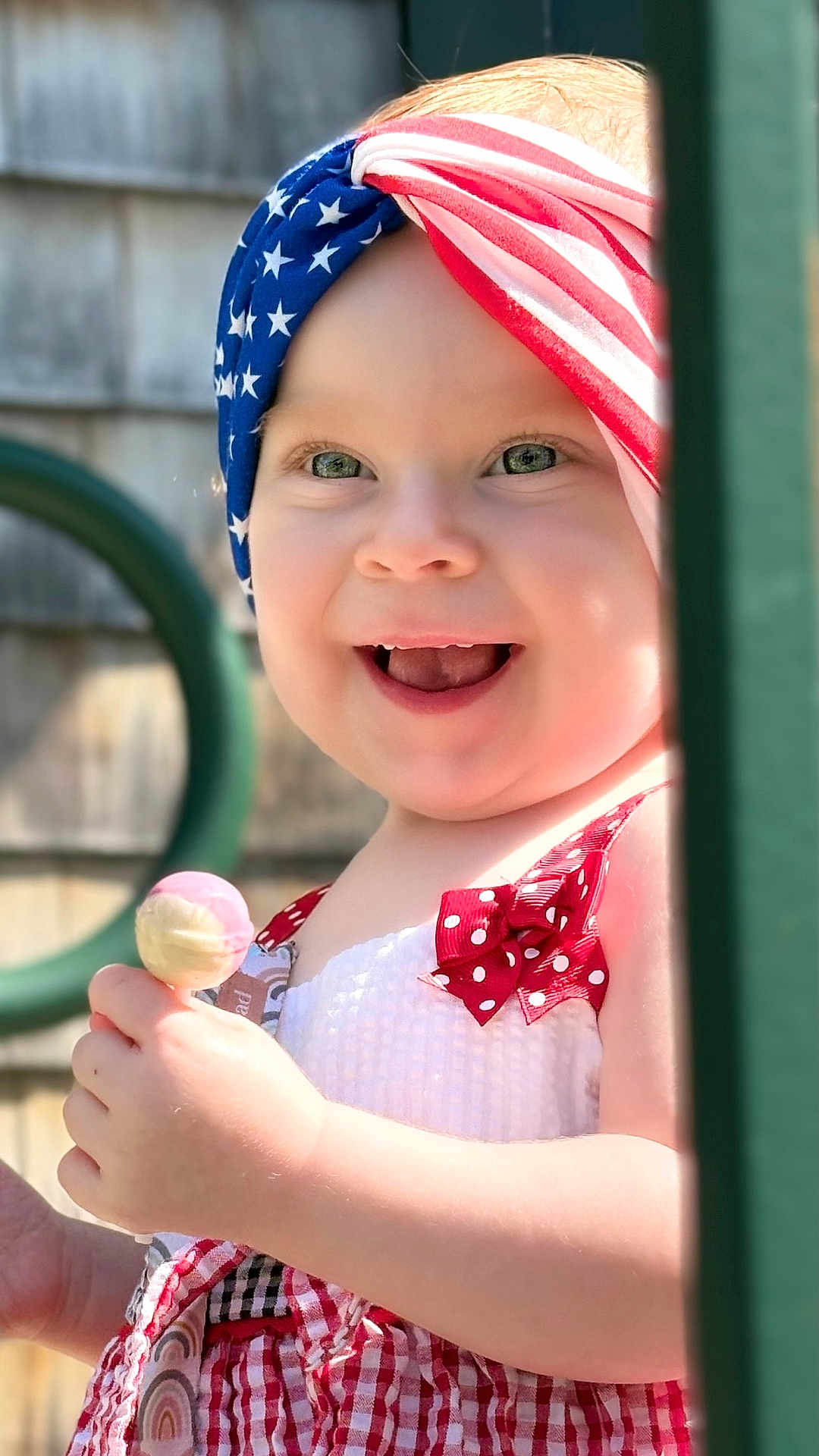 Naveigh is registered to the contest to win money with this photo: toddler, child, smiling, happy, headband, american_flag, lollipop, outdoor, sunlight, playground, red_dress, polka_dot, baby, face, portrait, summer, cute, young_child, hand, play