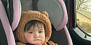 Maeve is registered to the contest to win money with this photo: baby, brown_clothing, car_interior, car_seat, child, cute, face, foot, fuzzy_clothing, hand, head, infant, onesie, outdoor_view, safety, seat, seatbelt, serious_expression, vehicle, window