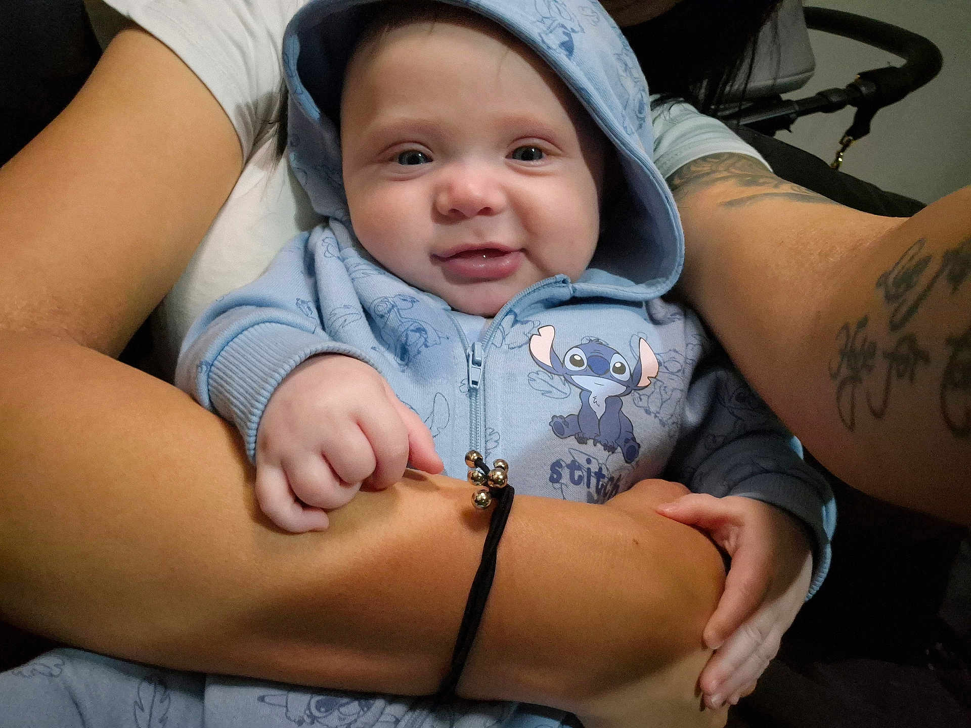 Riley joined the competition — help win amazing prizes! baby, infant, smiling, hoodie, blue_hoodie, hands, arms, tattoo, bracelet, stroller, closeup, portrait, cute, cheeks, zipper, eye_contact, holding, fabric_pattern, indoors, parental_embrace