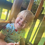 Mason is registered to the contest to win money with this photo: blonde_hair, casual, child, cute, daylight, face, hand, happy, natural_light, outdoor, patterned_clothing, playful, porch, short_sleeve_shirt, sitting, smiling, snack, sunlight, toddler, wooden_portrait