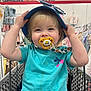 toddler, child, pacifier, blue_hat, shopping_cart, baby_clothing_store, clothing, baby, cute, blonde_hair, short_sleeves, colorful, retail, indoor, person, seat, holding_hat, curious, smiling, accessories