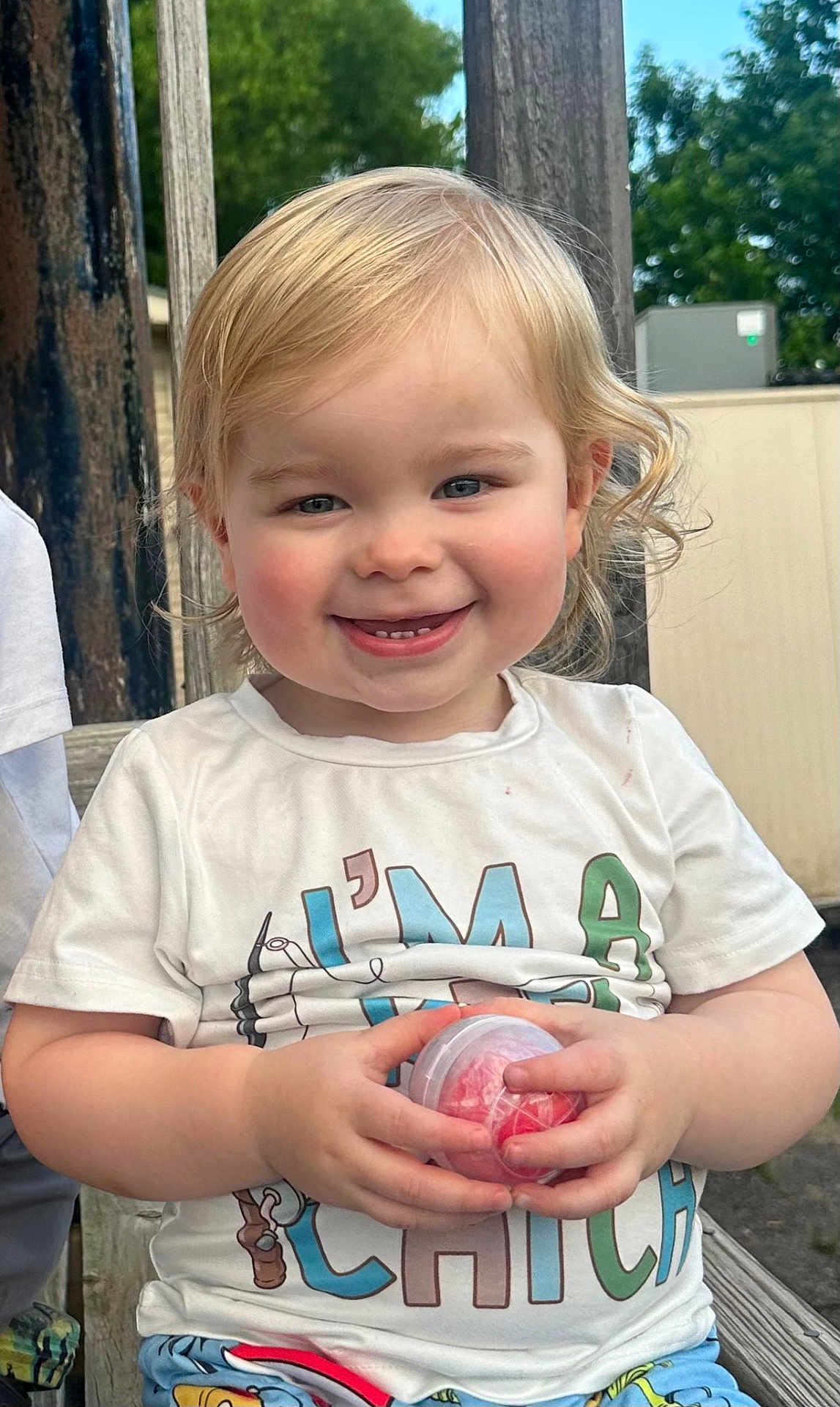 Mason joined the competition — help win amazing prizes! toddler, child, smiling, outdoor, bench, blonde_hair, rosy_cheeks, white_tshirt, colorful_letters, holding_object, plastic_container, happy, portrait, daylight, casual_clothing, wooden_bench, nature_background, cute, playful, person