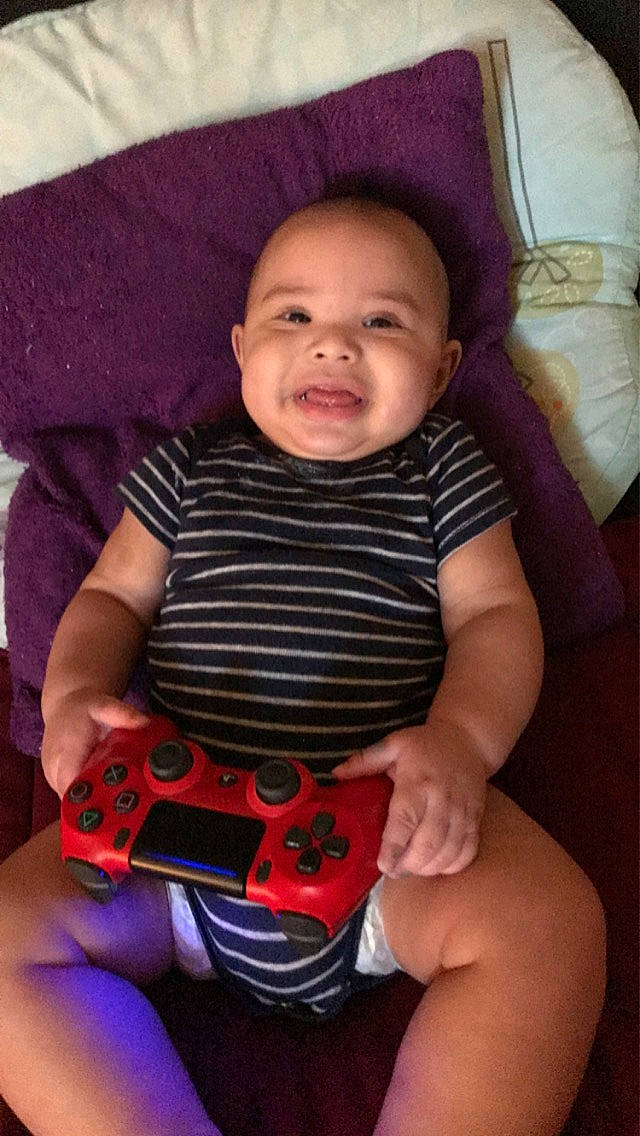 Armon is registered to the contest to win money with this photo: baby, black, cheek, comfort, cool, eye, face, finger, game_controller, iris, lip, mouth, nose, orange, organ, person, pink, red, skin, smile