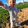 child, toddler, smiling, striped_shirt, sneakers, pants, outdoor, park, grass, blue_sky, sunlight, portrait, closeup, candid, happy, reaching, playground_surface, bokeh, expression, daytime