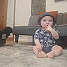 Zack joined the competition — help win amazing prizes! baby, child, hat, sitting, floor, rug, indoor, living_room, couch, pillow, hand, face, expression, clothing, furniture, foot, headwear, person, curious, toddler