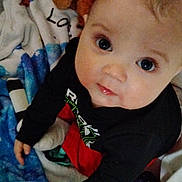 Zack is registered to the contest to win money with this photo: baby, child, infant, blanket, blue, stars, clothing, face, eyes, indoors, looking_up, person, cute, soft, young, sitting, curious, black_shirt, red_pants, home