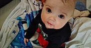 Zack is registered to the contest to win money with this photo: baby, black_shirt, blanket, blue, child, clothing, curious, cute, eyes, face, home, indoors, infant, looking_up, person, red_pants, sitting, soft, stars, young