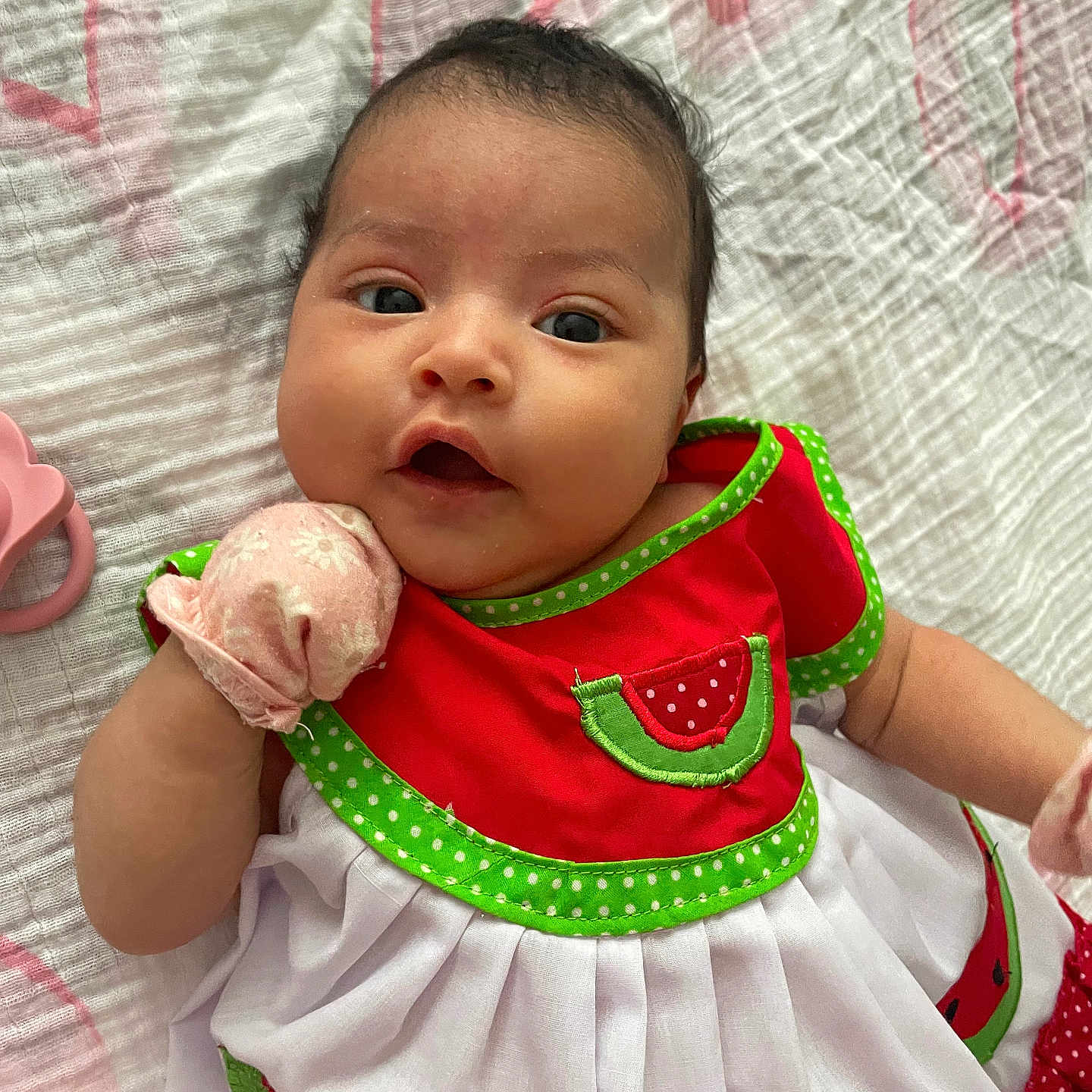 Sophia is registered to the contest to win money with this photo: adorable, baby, blanket, child, closeup, colorful_clothing, cute, dress, expression, face, hand, indoors, infant, lying_down, pink_mitten, portrait, skin, soft_texture, watermelon_theme, young_child
