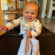 Finley is registered to the contest to win money with this photo: baby, blanket, child, clothing, cozy, decor, face, furniture, happy, high_chair, home, indoor, lamp, mirror, person, plant, portrait, smiling, table, wood_floor