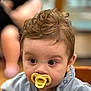 Cooper joined the competition — help win amazing prizes! baby, pacifier, curly_hair, close_up, indoor, child, face, eyes, clothing, person, infant, cute, portrait, young_child, blurry_background, sitting, soft_light, skin, head, expression