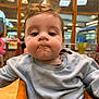 Cooper is registered to the contest to win money with this photo: baby, child, face, messy_hair, food_on_face, blue_sweater, indoor, chair, expressionless, person, blurred_background, wooden_furniture, light, window, people, casual_clothing, closeup, seated, young_child, portrait