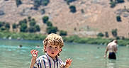 Cooper joined the competition — help win amazing prizes! blurred_background, casual_clothing, child, curly_hair, fun, lake, mountain, nature, outdoor, person, playing, recreation, scenic, striped_clothing, summer, sunlight, wading, water, waterfront, young_child