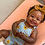 baby, smiling, child, romper, sunflower, headband, bow, curly_hair, peach_cushion, happy, infant, cute, indoor, skin, hand, face, person, clothing, lying_down, adorable