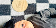 Layla is registered to the contest to win money with this photo: baby, infant, face, eyes, headband, black_clothing, blanket, checkered_pattern, lying_down, portrait, cute, child, soft_texture, indoor, expression, young, closeup, person, head, skin