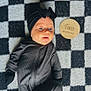 Layla is registered to the contest to win money with this photo: baby, infant, black_outfit, headband, checkered_blanket, wooden_sign, two_months, face, blue_eyes, lying_down, cozy_clothing, milestone, portrait, cute, soft_lighting, indoor, child, newborn, expression, zipped_outfit
