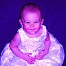baby, child, dress, white_dress, smiling, sitting, portrait, face, person, infant, cute, happy, hands, young_child, purple_background, fabric, clothing, indoor, expression, baby_girl
