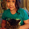 animal, cabinet, casual, cat, child, cozy, curly_hair, furniture, girl, holding, home, indoor, pet, portrait, shelf, short_sleeve_shirt, sitting, smiling, tabby_cat, young
