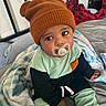 Amarion joined the competition — help win amazing prizes! baby, child, pacifier, hat, knit_hat, blanket, bed, bedding, clothing, sitting, indoors, person, cute, face, looking_up, soft, warm, comfort, expression, young