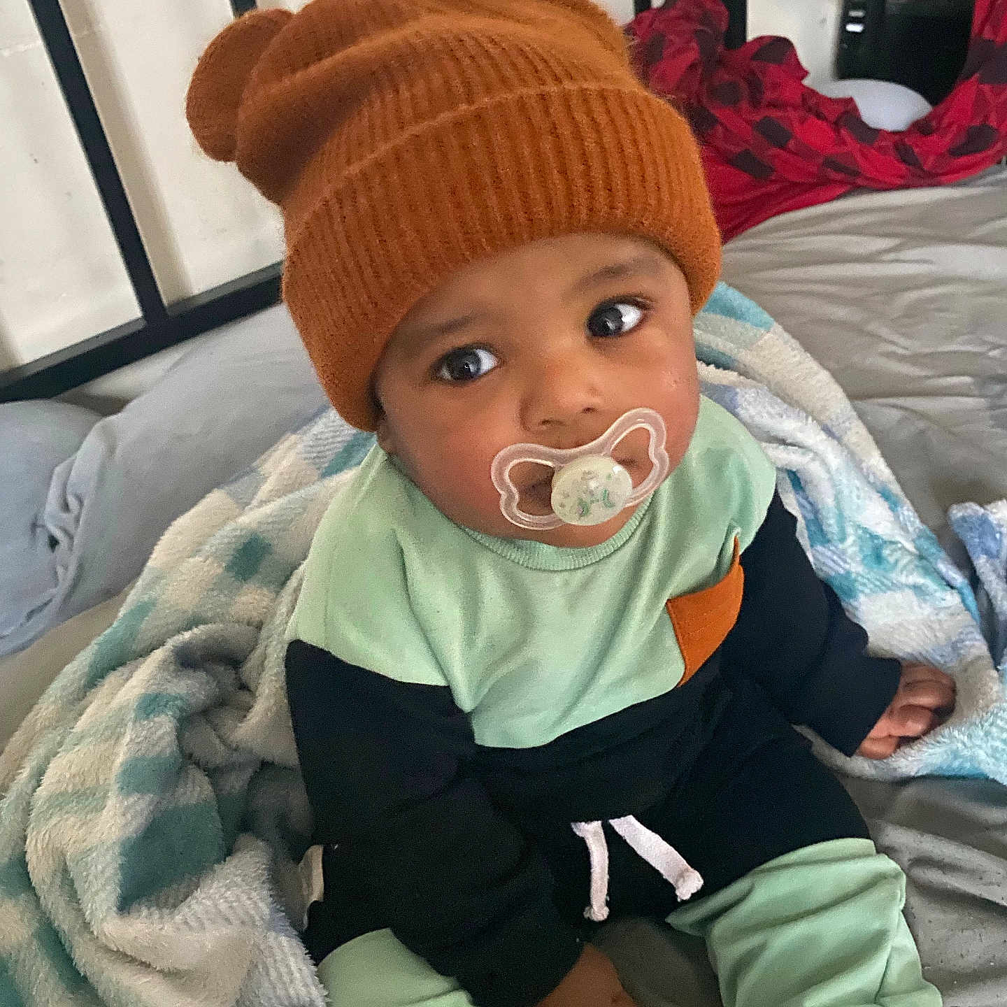 Amarion joined the competition — help win amazing prizes! baby, child, pacifier, hat, knit_hat, blanket, bed, bedding, clothing, sitting, indoors, person, cute, face, looking_up, soft, warm, comfort, expression, young