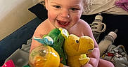 Jeremiah Cox is registered to the contest to win money with this photo: toddler, child, baby, curly_hair, smiling, stuffed_animals, toys, bottle, bed, blanket, indoor, happy, playful, person, cuddly_toys, colorful, cute, young_child, infant, room