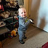 Jeremiah Cox joined the competition — help win amazing prizes! child, toddler, indoor, carpet, toys, shelf, clothing, gloves, door, wall, floor, person, standing, footwear, plush_toy, cable, blanket, furniture, room, happy