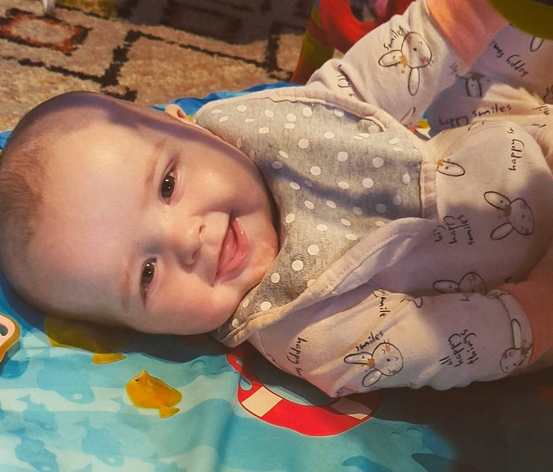 Amara is registered to the contest to win money with this photo: baby, baby_toddler_clothing, cheek, child, eye, facial_expression, flooring, fun, happy, head, iris, lip, mouth, nose, pattern, person, skin, sleeve, smile, toddler