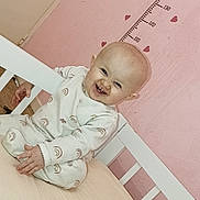 Serena a rejoint le concours — aidez-le/la à gagner de superbes lots ! baby, child, crib, onesie, pink_wall, height_chart, heart_shapes, smiling, happy, indoors, bed, mattress, toddler, cute, person, infant, clothing, furniture, playful, room