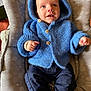 baby, blue_hoodie, knitted_clothing, wooden_buttons, baby_seat, patterned_cushion, infant, cute, smiling, child, cozy, portrait, indoor, sitting, clothing, face, hands, feet, warm, comfort