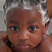 Arys is registered to the contest to win money with this photo: baby, child, bath, foam, shampoo, curly_hair, water, skin, face, eyes, expression, hand, adult_hand, wet, closeup, portrait, cute, indoors, personal_care, infant