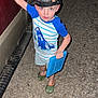 child, boy, cap, hat, blue_shirt, striped_shirt, shark_graphic, green_slippers, dinosaur_slippers, tablet, vehicle, red_vehicle, night, flash_photo, gravel, outdoor, standing, toy, play, casual_clothing