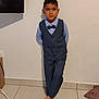 child, boy, suit, bow_tie, barefoot, standing, indoor, tile_floor, wall, portrait, formal_wear, person, casual_pose, short_hair, blue_shirt, vest, pants, looking_at_camera, calm_expression, home