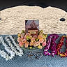 cat_photo, memorial, flower_lei, beach, sand, blue_blanket, wooden_box, flowers, pink_flowers, yellow_flowers, purple_flowers, white_flowers, shade, outdoor, remembrance, pet_memorial, lei_garlands, tribute, nature, serene