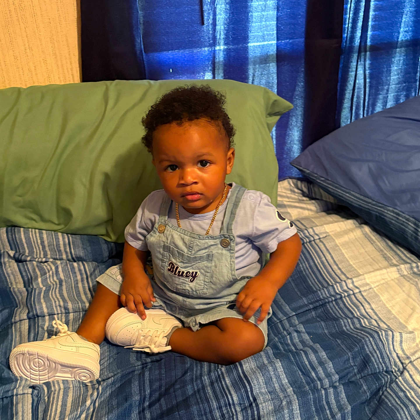Zechariah joined the competition — help win amazing prizes! child, toddler, baby, portrait, sitting, bedroom, bed, pillow, curtains, overalls, t_shirt, necklace, sneakers, striped_bedding, curly_hair, serious_expression, indoors, furniture, cozy, photography