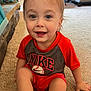 baseball, carpet, casual, child, clothing, face, furniture, happy, home, indoor, light, nike, person, red_shirt, shorts, sitting, smiling, toddler, toy, young_child
