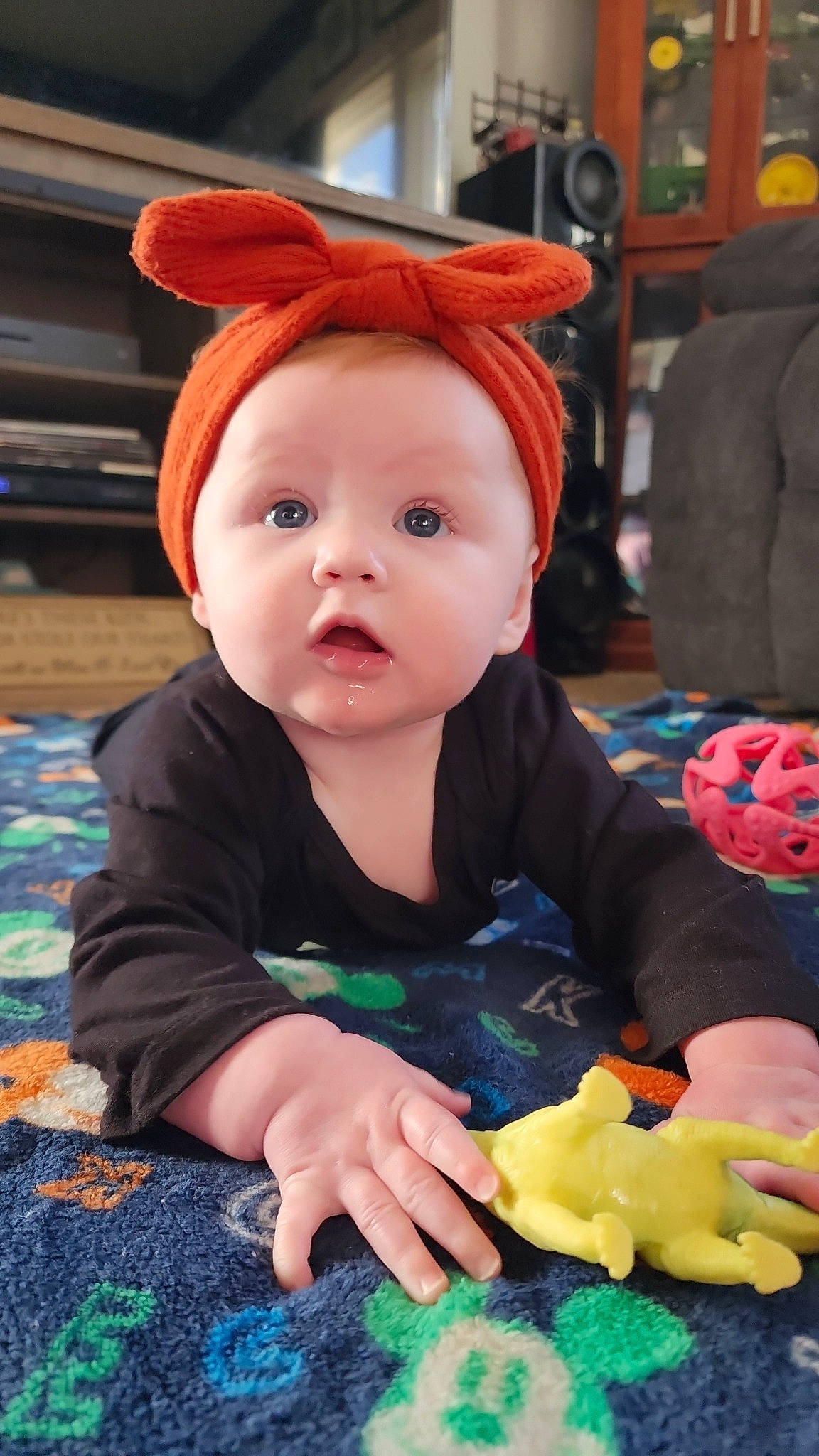 Kinze is registered to the contest to win money with this photo: baby, baby_toddler_clothing, cheek, child, comfort_food, costume_hat, fashion_accessory, flooring, fun, green, orange, person, photograph, play, room, sitting, snapshot, surprise, textile, toddler