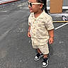 toddler, child, braided_hair, sunglasses, shorts, shirt, smiley_face_pattern, sneakers, bracelet, necklace, earrings, outdoor, paved_driveway, white_picket_fence, cardboard_box, tools, confident, fashionable, standing, side_profile