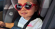 Catalina is registered to the contest to win money with this photo: toddler, child, car_seat, sunglasses, strawberry, white_tshirt, nike, bracelet, smile, hair_bun, seatbelt, car_interior, sunlight, cute, fashion, portrait, safety, young_child, happy, casual