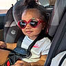 toddler, child, car_seat, sunglasses, strawberry, white_tshirt, nike, bracelet, smile, hair_bun, seatbelt, car_interior, sunlight, cute, fashion, portrait, safety, young_child, happy, casual