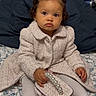 Catalina is registered to the contest to win money with this photo: toddler, child, pigtails, coat, purse, pearl_handle, white_tights, white_shoes, bedspread, floral_pattern, indoor, portrait, cute, fashion, seated, curly_hair, young_child, serious_expression, small_bag, cozy_clothing