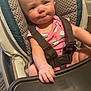 Keira is registered to the contest to win money with this photo: baby, high_chair, child, pink_clothing, cupcake_pattern, straps, hand, face, expression, indoor, furniture, tray, person, seat, young, infant, curious, skin, arm, head