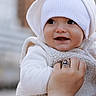 Ostap is registered to the contest to win money with this photo: adult_hand, baby, bracelet, building, child, closeup, cozy, cute, happy, hat, holding, hood, infant, outdoor, person, portrait, ring, smiling, urban, white_clothing