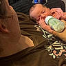 baby, bottle, feeding, infant, person, adult, brown_shirt, text, hand, face, sleepy, indoor, closeup, holding, cuddle, skin, hair, relaxation, comfort, blanket