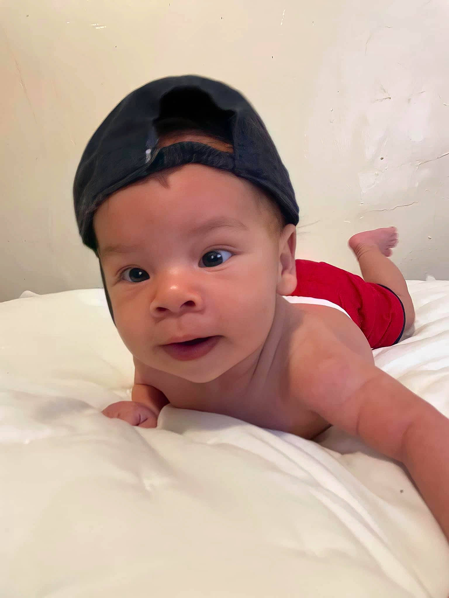 Lucian is registered to the contest to win money with this photo: baby, baby_toddler_clothing, cap, cheek, child, comfort, flesh, fun, hair_accessory, happy, headwear, human_body, linens, person, portrait_photography, room, sitting, smile, thumb, toddler