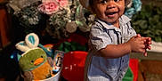 Omari joined the competition — help win amazing prizes! toddler, child, smiling, hat, romper, flip_flops, wooden_floor, christmas_tree, holiday, decorations, toys, stuffed_animal, bucket, ribbon, flower, indoor, happy, person, clapping, festive
