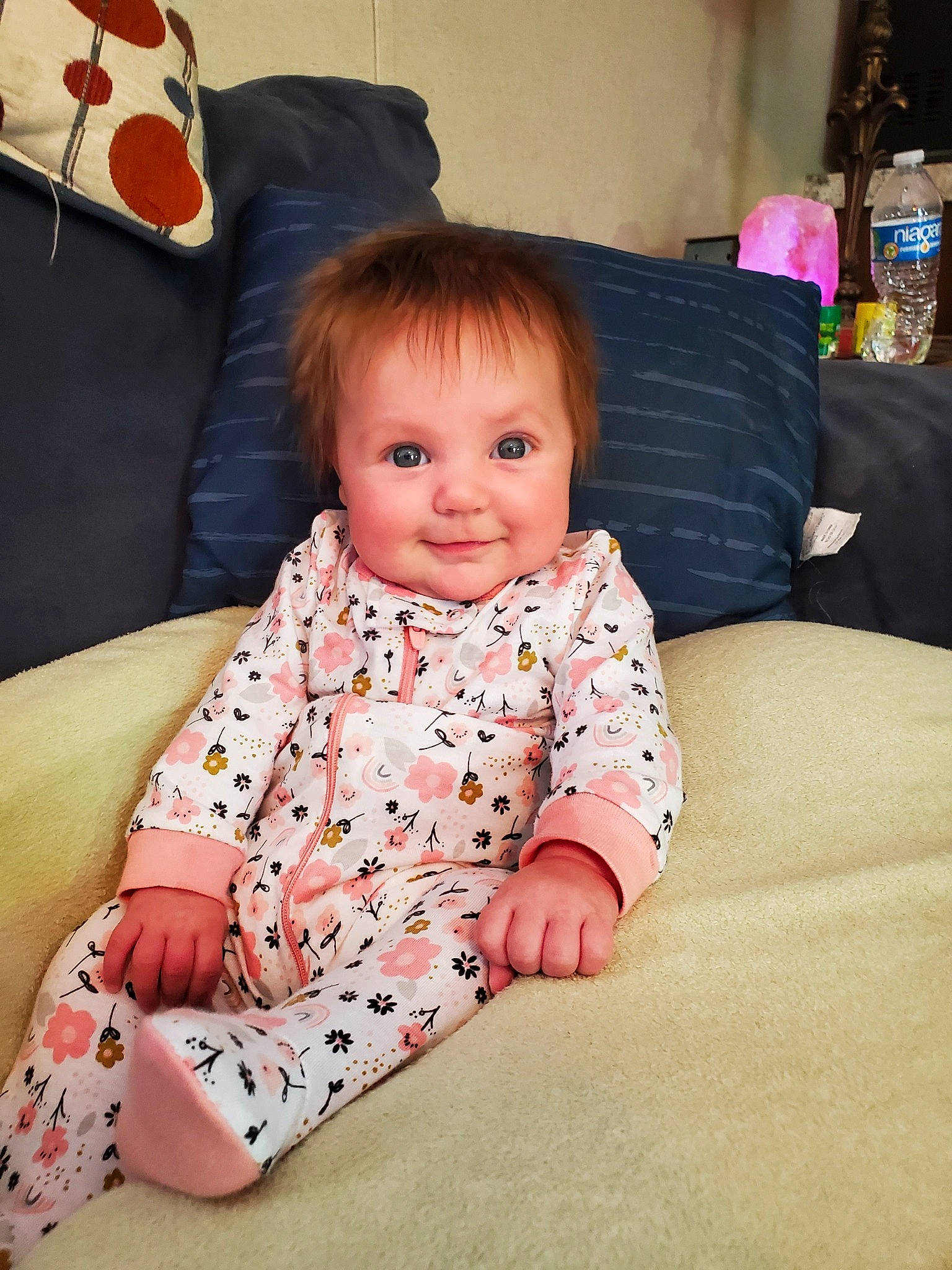 Adelynn is registered to the contest to win money with this photo: baby, baby_toddler_clothing, cheek, child, comfort, couch, eye, fun, happy, joy, lap, leg, linens, living_room, mammal, person, pillow, sitting, skin, sleeve