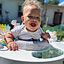 baby, walker, smiling, curly_hair, outdoor, sunny, daylight, happy, child, person, clothing, white_shirt, toy, furniture, garden, house, background, blurred_background, skin, expression