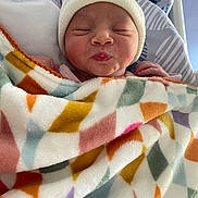 Louise a rejoint le concours — aidez-le/la à gagner de superbes lots ! baby, newborn, blanket, hat, bed, sleeping, puckered_lips, infant, colorful, geometric_pattern, cozy, cute, resting, closeup, soft, child, person, warm, indoors, peaceful