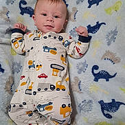 Eli joined the competition — help win amazing prizes! baby, infant, onesie, blanket, dinosaur_pattern, cute, smiling, lying_down, toddler, child, happy, clothing, face, person, indoor, soft_texture, colorful, patterned, sleepwear, young_child