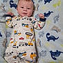 baby, infant, onesie, blanket, dinosaur_pattern, cute, smiling, lying_down, toddler, child, happy, clothing, face, person, indoor, soft_texture, colorful, patterned, sleepwear, young_child